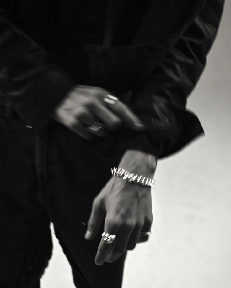 Black-and-white close-up of hands in motion wearing silver rings and a chunky bracelet.