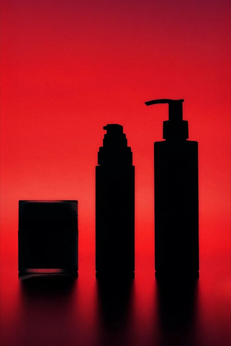 Three skincare containers in black silhouette against a glowing red backdrop.